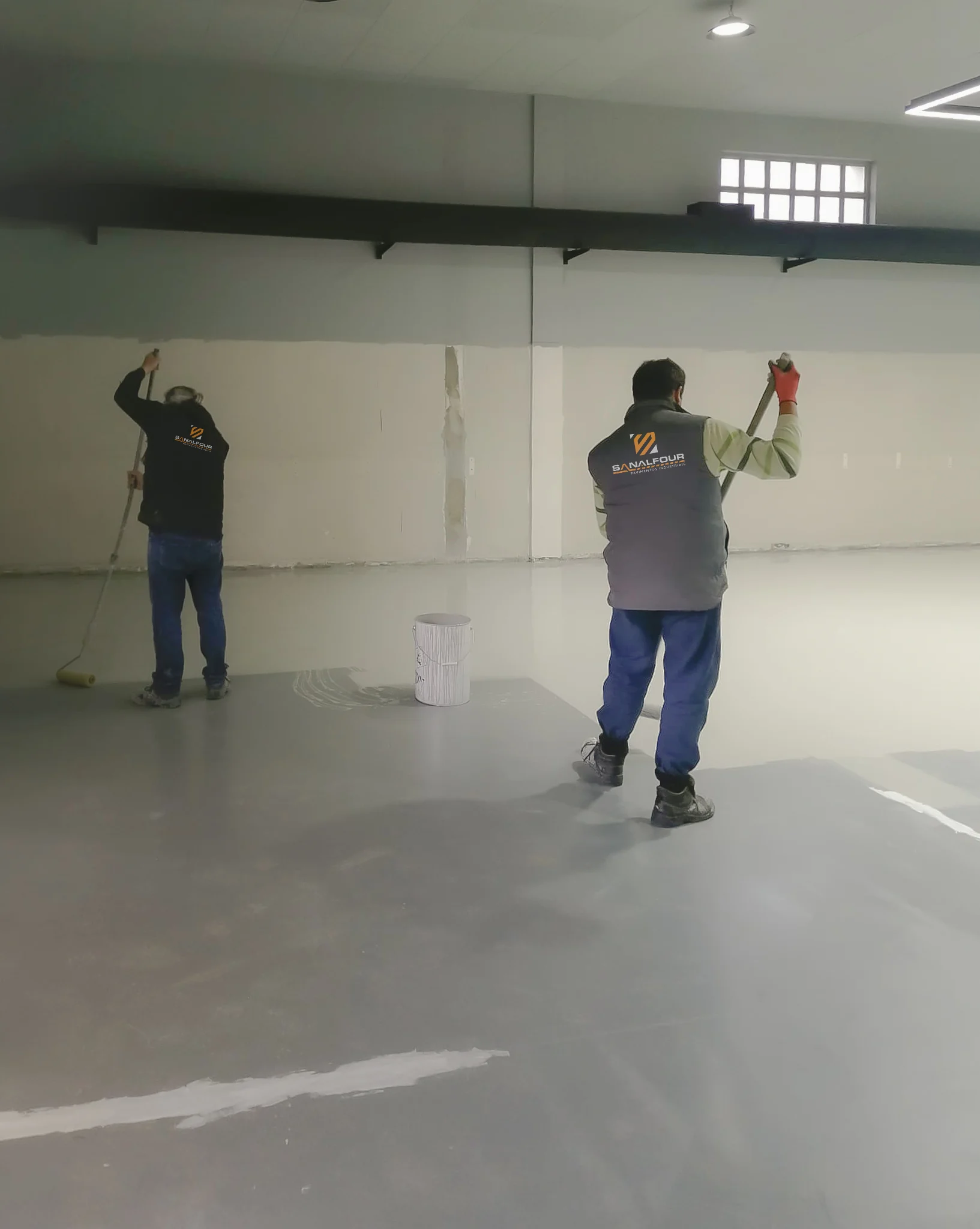 Dois técnicos a aplicar resina epóxi com rodo no pavimento de uma cantina